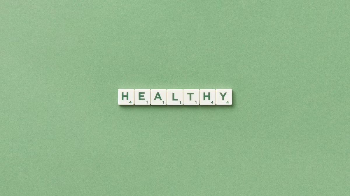 Scrabble tiles spelling the word 'healthy' on a light green background, top view.
