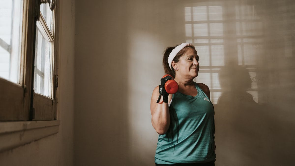 Middle-aged woman in workout attire lifting a dumbbell indoors, promoting fitness and healthy lifestyle.